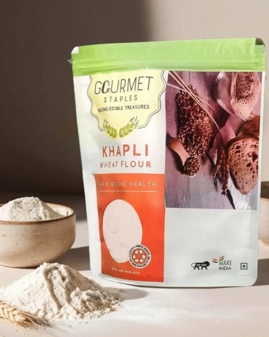 Khapli wheat flour packet with bowl and pile of flour on a light surface, healthy staple food